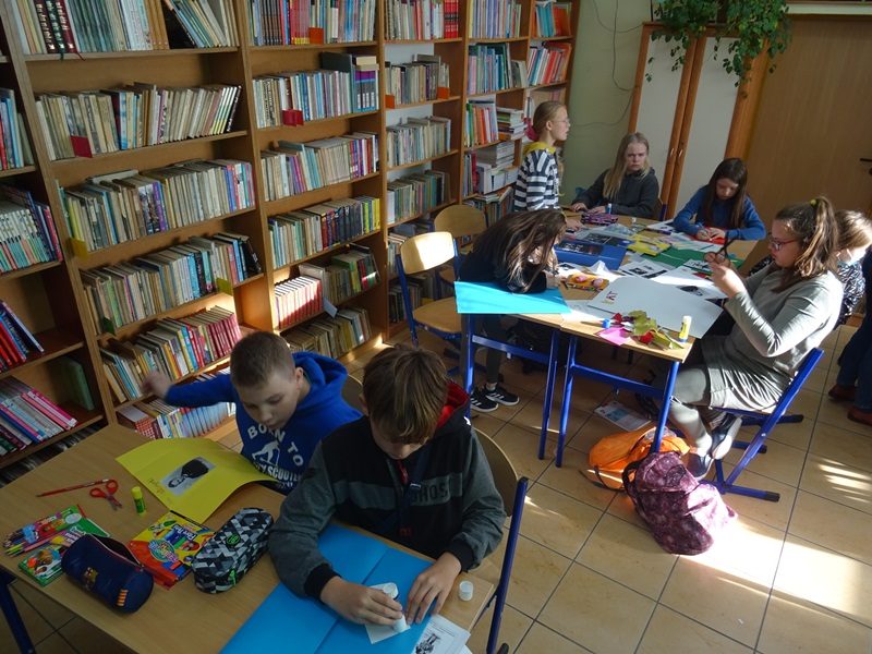 Biblioteka szkolna. Uczniowie siedzą przy stolikach i przygotowują lapbooki.