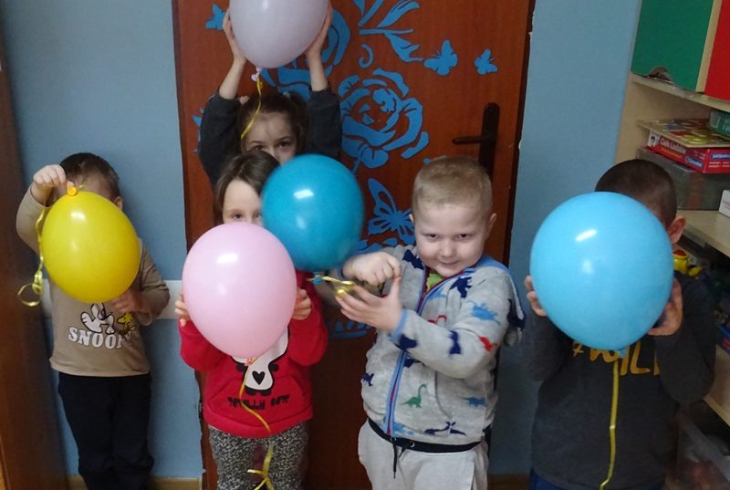 Klasa przedszkolna. Dzieci stoją przy drzwiach i trzymają kolorowe baloniki.