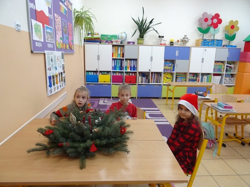 Sala lekcyjna. Trzech uczniów siedzi przy ławce. Na ławce stoi stroik świąteczny.