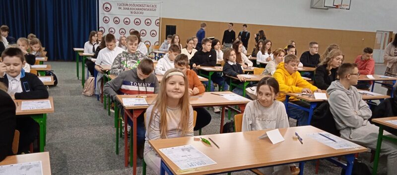 Sala gimnastyczna w I Liceum Ogólnokształcącym w Olecku. Przy stolikach siedzą uczestnicy konkursu.