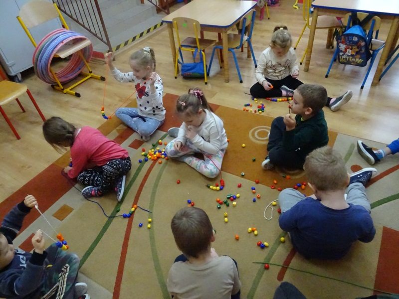 Sala przedszkolna. Dzieci siedza na podłodze i bawią się kolorowymi kulkami.