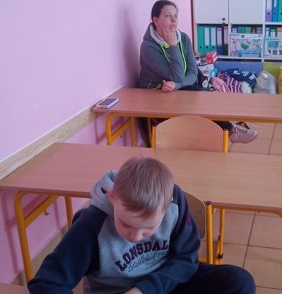 Sala lekcyjna. Przy ławkach siedzą uczeń i rodzic.