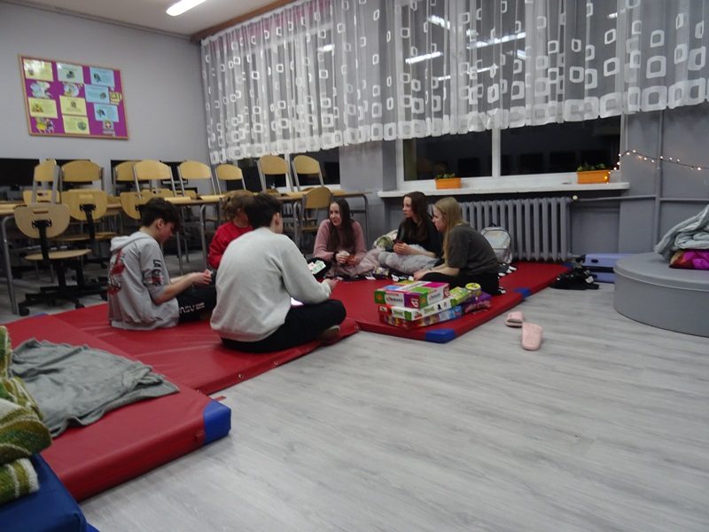 Sala lekcyjna. Uczniowie siedzą na materacach i grają w gry planszowe.
