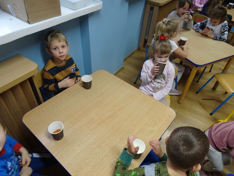 Sala przedszkolna. Dzieci siedzą przy stolikach i piją napój jabłkowy.