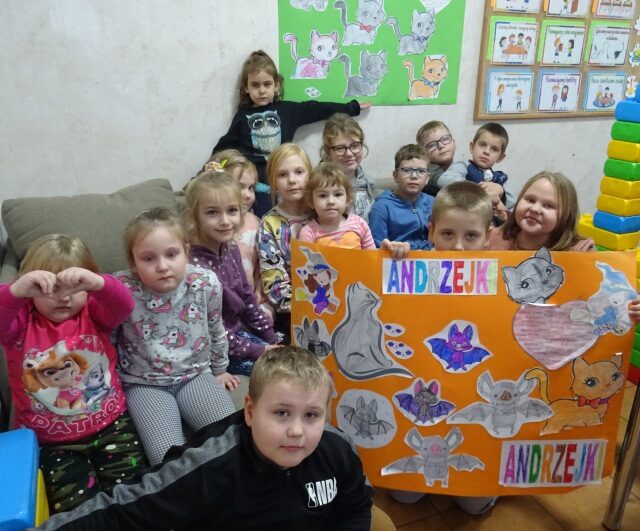 Świetlica opiekuńczo-wychowawcza. Dzieci siedzą na kanapie. Uczeń trzyma plakat z napisem Andrzejki.