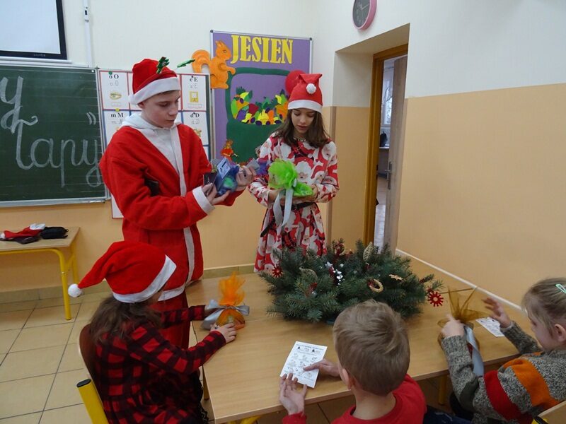 Sala lekcyjna. Wizyta Mikołaja i Śnieżynki w klasie. Uczniowie otrzymują prezenty.