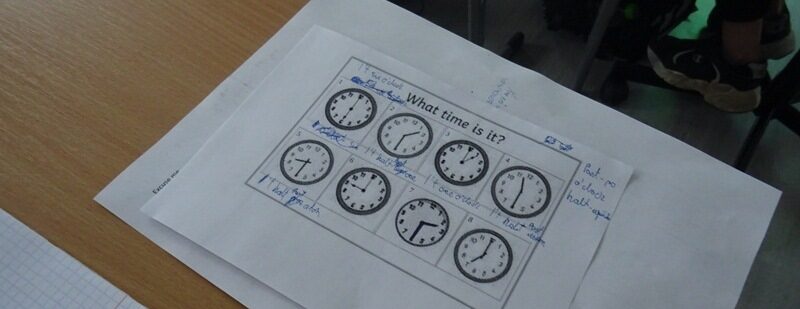 Sala lekcyjna. Na stoliku leży kartka z informacją na temat określania czasu w języku angielskim.