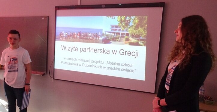 Sala lekcyjna. Uczniowie stoją przy ekranie. Na ekranie slajd o nazwie: Wizyta partnerska w Grecji.