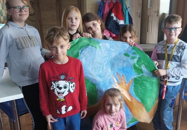 Pomieszczenie świetlicy. Dzieci stoją przy plakacie, przedstawiającym Ziemię.