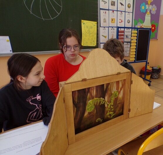 Sala lekcyjna. Uczniowie siedzą przy teatrzyku - skrzynce i prezentują ilustracje.
