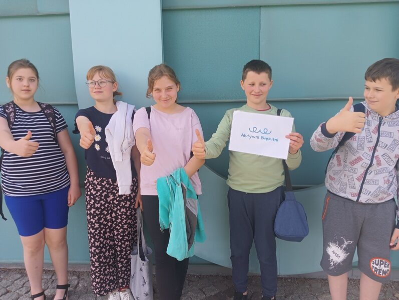 Aquapark w Suwałkach. Uczniowie stoją przy ścianie. Jeden z uczniów trzyma logo Aktywni Błękitni.