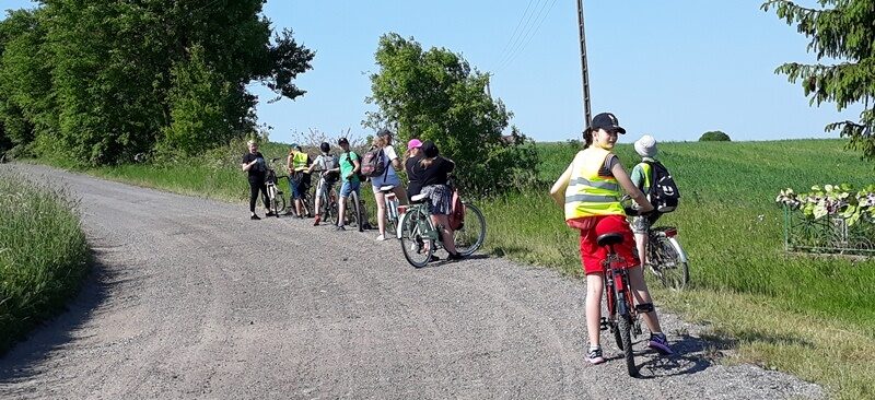 Droga w Judzikach. Uczniowie i nauczycielka na rowerach. Rowerzyści odpoczywają.
