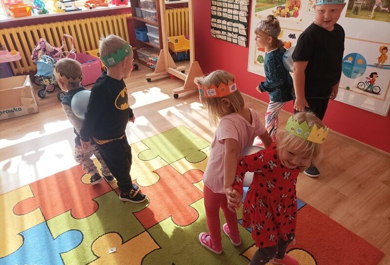 Sala dydaktyczna. Dzieci bawią się trzmając plecami napompowane baloniki. 