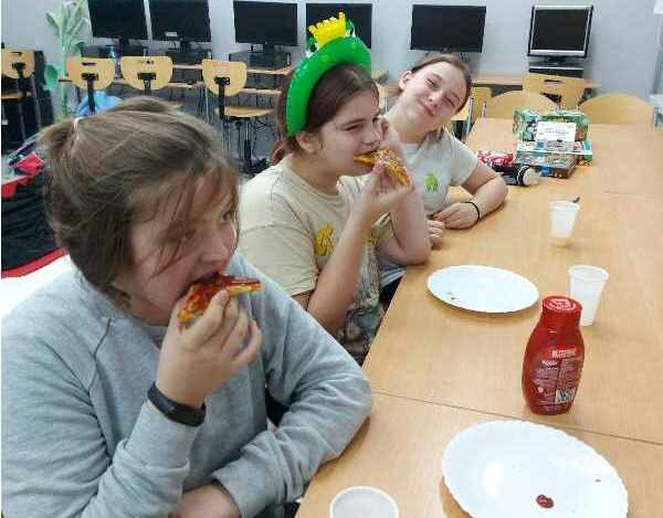 Sala lekcyjna. Uczennice siedzą przy stoliku i jedzą pizzę.