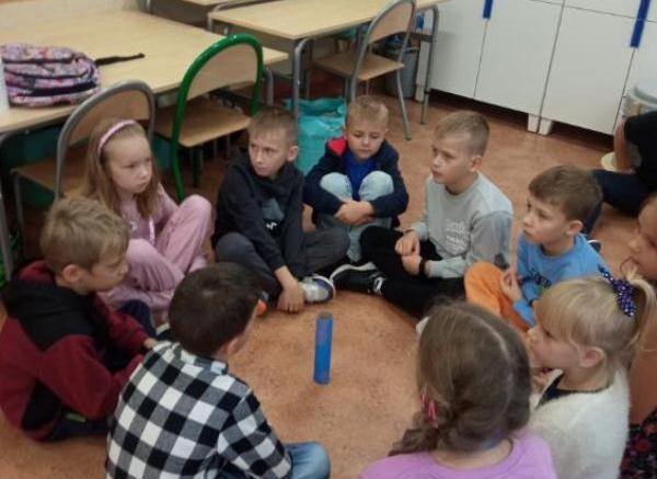 Szkoła Podstawowa nr 2 w Olecku. Sala dydaktyczna. Dzieci siedzą na podłodze w kółku. Przed nimi pośrodku stoi niebieski klocek.