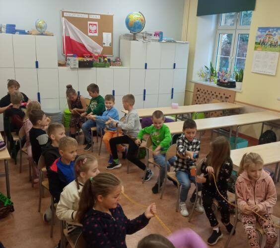 Szkoła Podstawowa nr 2 w Olecku. Sala dydaktyczna. Dzieci siedzą na krzesłach jedno za drugim i trzymają linkę.