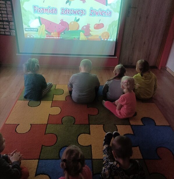 Sala przedszkolna. Dzieci siedzą na dywanie i oglądają film.