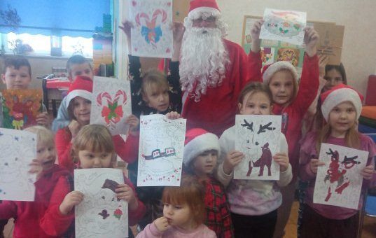 Świetlica. Dzieci stoją przy Mikołaju i trzymają rysunki.