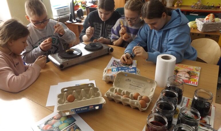 Biblioteka szkolna. Uczniowie siedzą przy stołach i malują jajka.
