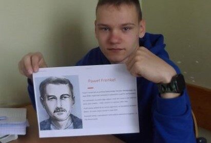 Sala dydaktyczna. Uczeń siedzi przy ławce i trzyma kartkę z informacjami o getcie warszawskim.