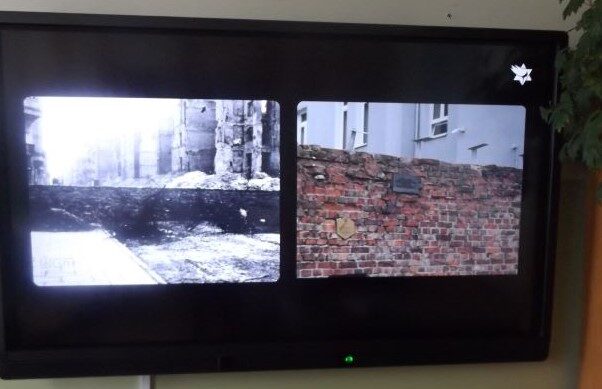 Sala dydaktyczna. Slajd na tablicy interaktywnej przedstawiający fragment muru getta warszawskiego.