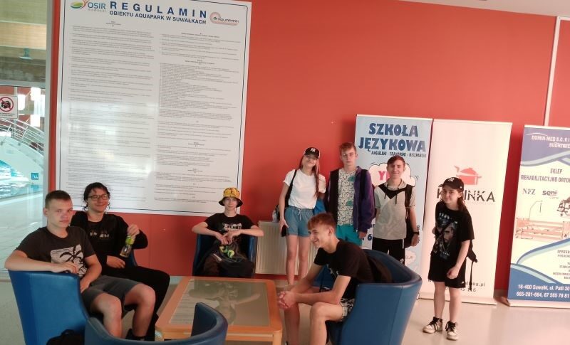 W Aquaparku w Suwałkach. Uczniowie siedzą na fotelach i stoją przy ścianie.