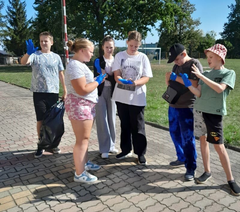 Posesja szkolna. Uczniowie w niebieskich rękawiczkach stoją obok siebie. 