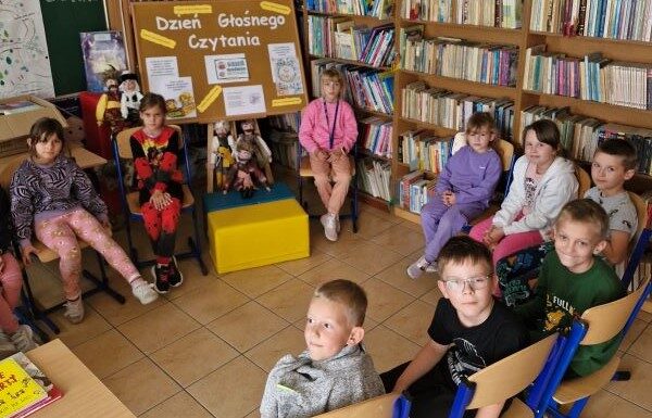 Biblioteka szkolna. Uczniowie siedzą na krzesełkach.