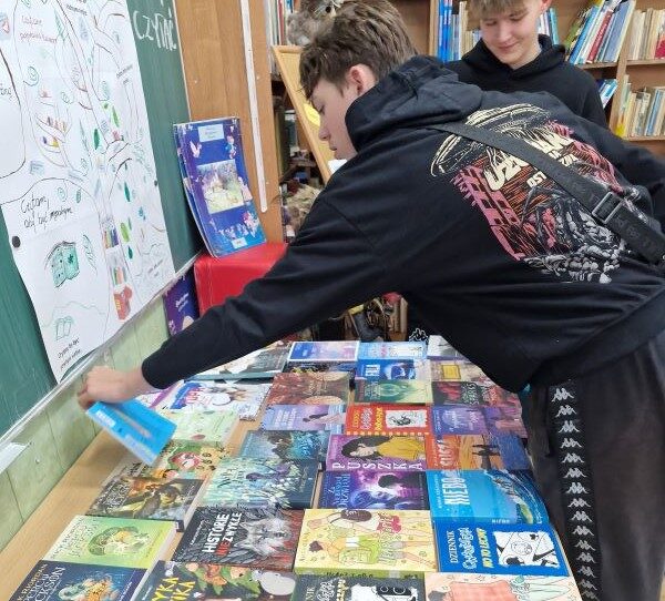 Biblioteka szkolna. Uczniowie oglądają książki, które leżą na stole.